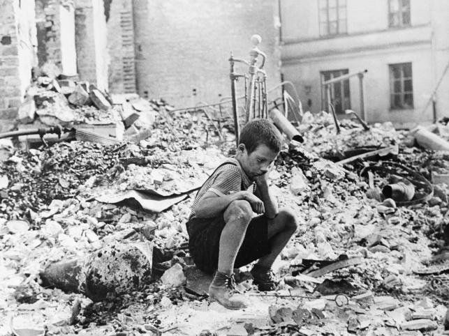 Warszawa wrzesień 1939, mały chłopiec w przerwie pomiędzy nalotami siedzi na ruinach swojego domu zbombardowanego przez nimieckie lotnictwo