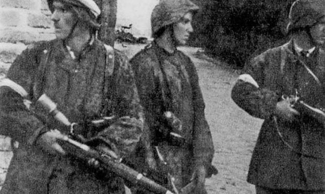 Patrol z II plutonu "Alek" 2. kompanii "Rudy" batalionu "Zośka" 5 sierpnia 1944 r. na Gęsiówce. Od lewej stoją: Wojciech Omyła "Wojtek", Juliusz Bogdan Deczkowski "Laudański" i Tadeusz Milewski "Ćwik". Milewski poległ na terenie "Gęsiówki" w dniu zrobienia tego zdjęcia; Omyła zginie trzy dni później. W chwilę po zrobieniu tego zdjęcia, w mur nad głowami powstańców uderzył niemiecki pocisk karabinowy - nikomu nic się nie stało